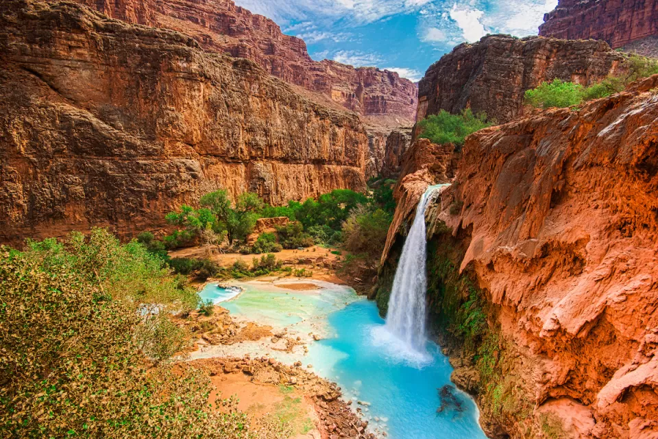 View of Havasu Falls with bright turquoise water and a canyon winding through red vertical cliffs in the Grand Canyon